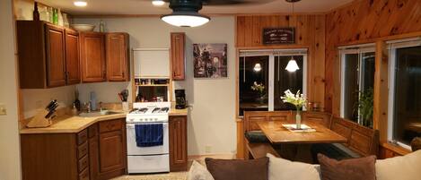 A compact kitchen with wooden cabinets, a stove, and a dining area with a table and chairs.