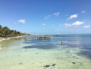 A beach with clear shallow waters, a wooden pier, and a thatched-roof structure.