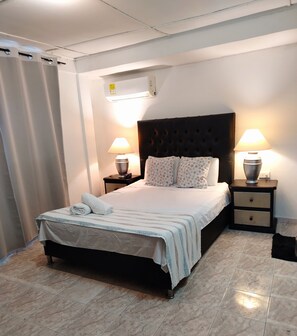 Ein Hotelzimmer mit einem Bett, zwei Nachttischen, einem Kopfteil und einem Fenster mit Vorhängen.