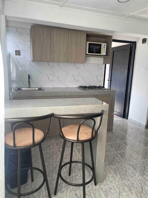 A compact kitchen with a built-in microwave, a gas stove, and a marble backsplash. There are two bar stools with cushioned seats. - Single Bedroom in the heart of Getsemani_302 (Cartagena)