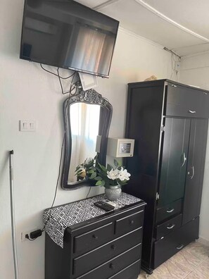 Ein Zimmer mit einem an der Wand montierten Fernseher, einem Schrank mit Schubladen, einem Spiegel und einem Kleiderschrank.