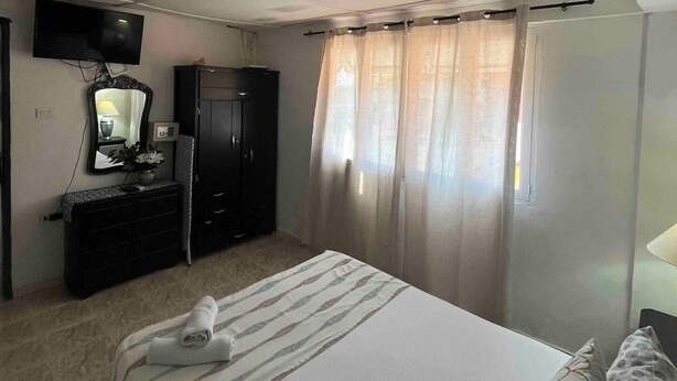 Un dormitorio con cama, armario, televisor y ventana con cortinas.