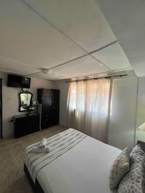 A bedroom with a bed, a wardrobe, a television, and a window with curtains.
