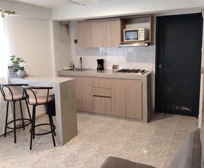 A compact kitchen with a microwave, gas stove, and bar stools. - Single Bedroom in the heart of Getsemani_302 (Cartagena)