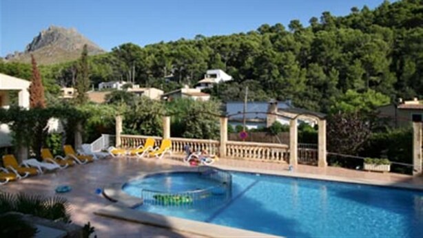 Una piscina con lettini prendisole e un gazebo, immersa nel verde e circondata da case.