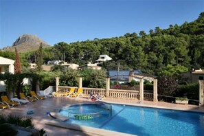 A swimming pool with lounge chairs and a gazebo, surrounded by greenery and houses.