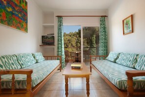 A living room with two sofas, a coffee table, and a TV on a shelf. - Apt. ROSALES, A/C in the bedroom, spacious living room with balcony. Pool, WIFI, close to the beach 400 m, max. 4 pax (Cala San Vicente)