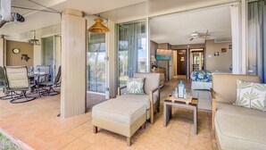 Un grand salon comprenant un canapé, un pouf et un ensemble de salle à manger. On y trouve également un téléviseur et une petite table avec une bouteille et des verres.
