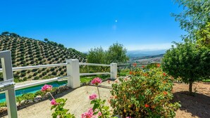Un jardín con piscina, cerca blanca y vista a un paisaje montañoso.