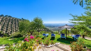 Una terraza con mobiliario exterior, una pérgola y vistas a viñedos y el paisaje distante.
