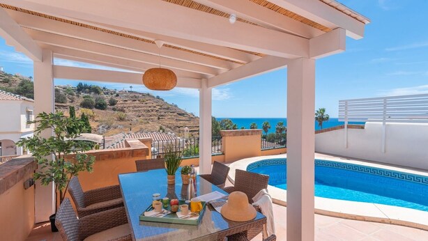 A covered outdoor seating area with a pool, overlooking a hillside and the sea. - Villa Claudia Nerja by Ruralidays (Málaga)
