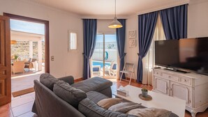 A living room with a sofa, TV, and a view of a pool and outdoor seating area. - Villa Claudia Nerja by Ruralidays (Málaga)