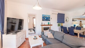 A living room with a flat-screen TV, a sofa, a coffee table, and a dining area with chairs and a table. - Villa Claudia Nerja by Ruralidays (Málaga)
