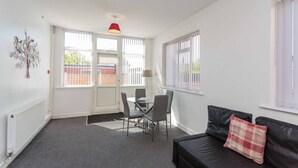 A modern living room with a black leather sofa, a glass dining table with chairs, and a red pendant light. - Cherry Property - Mulberry Suite (Blackpool)