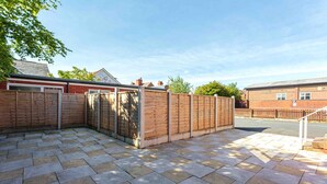 A paved patio area with a wooden fence, a brick wall, and a clear sky. - Cherry Property - Mulberry Suite (Blackpool)