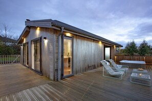 A wooden spa building with glass doors, a hot tub, and lounge chairs on a wooden deck. - Deer Leap, Strawberryfield Park -  a lodge that sleeps 2 guests  in 1 bedroom (Cheddar)