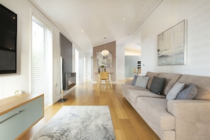 A spacious living room with a large sofa, a flat-screen TV mounted on the wall, and a dining area with a table and chairs. - Charterhouse, Strawberryfield Park -  a lodge that sleeps 2 guests  in 1 bedroom (Cheddar)