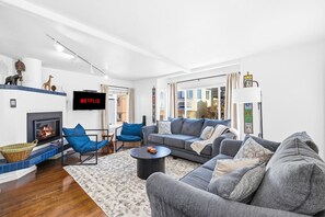 A modern living room with a fireplace, a sofa set, a coffee table, and a flat-screen TV mounted on the wall.