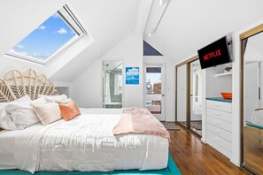 A bedroom with a bed, a TV, a wardrobe, and a skylight.
