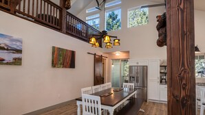 A dining area with a wooden table and white chairs, a staircase, and a view of the outdoors. - Half Dome Loft (Yosemite National Park)