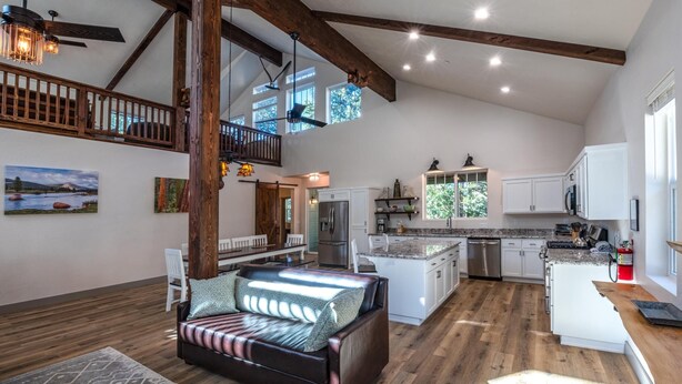 A spacious living area with a high ceiling, wooden beams, a sofa, a dining table, and a kitchen with white cabinets and a stainless steel refrigerator. - Half Dome Loft (Yosemite National Park)