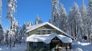 A snow-covered cabin with a porch, surrounded by tall, snow-laden trees. - Half Dome Loft (Yosemite National Park)