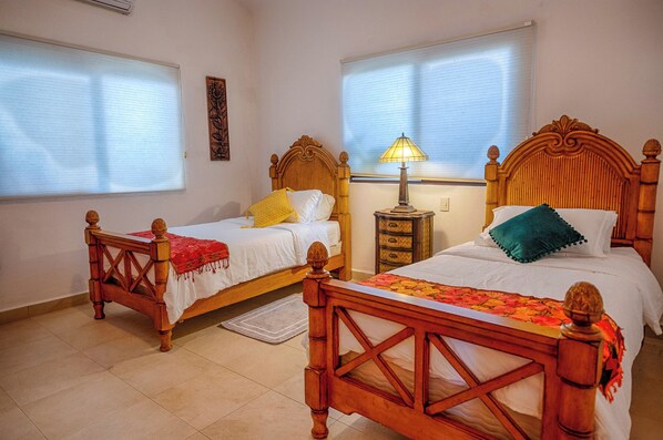 Una habitació d'hotel amb dos llits de fusta, una tauleta de nit amb una làmpada i una finestra amb persianes.