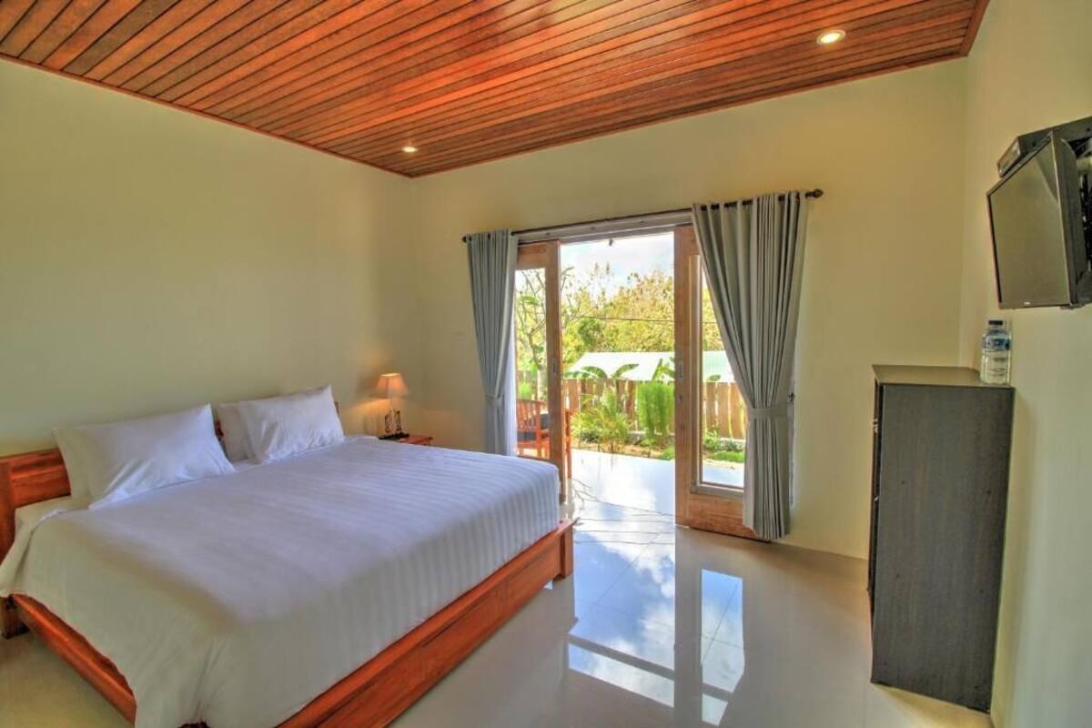 A bedroom with a wooden bed, a nightstand, a TV, and a sliding glass door leading to an outdoor area.