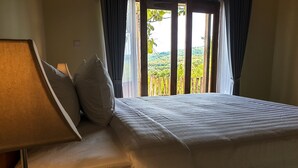 Una cama con cubre blanco, un control remoto y una lámpara en una mesita de noche.