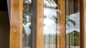 Una ventana con marcos de madera y vista a un jardín con palmeras y un sendero.