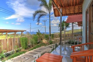 Eine Holzterrasse mit Glasbrüstung, die auf einen Garten mit Palmen und Meerblick führt.