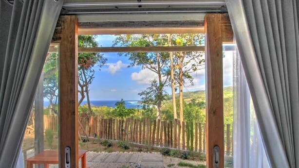 Vista desde el interior de una habitación con una puerta de madera que da a un espacio exterior con cerca de madera, un camino de piedra y una mesa.