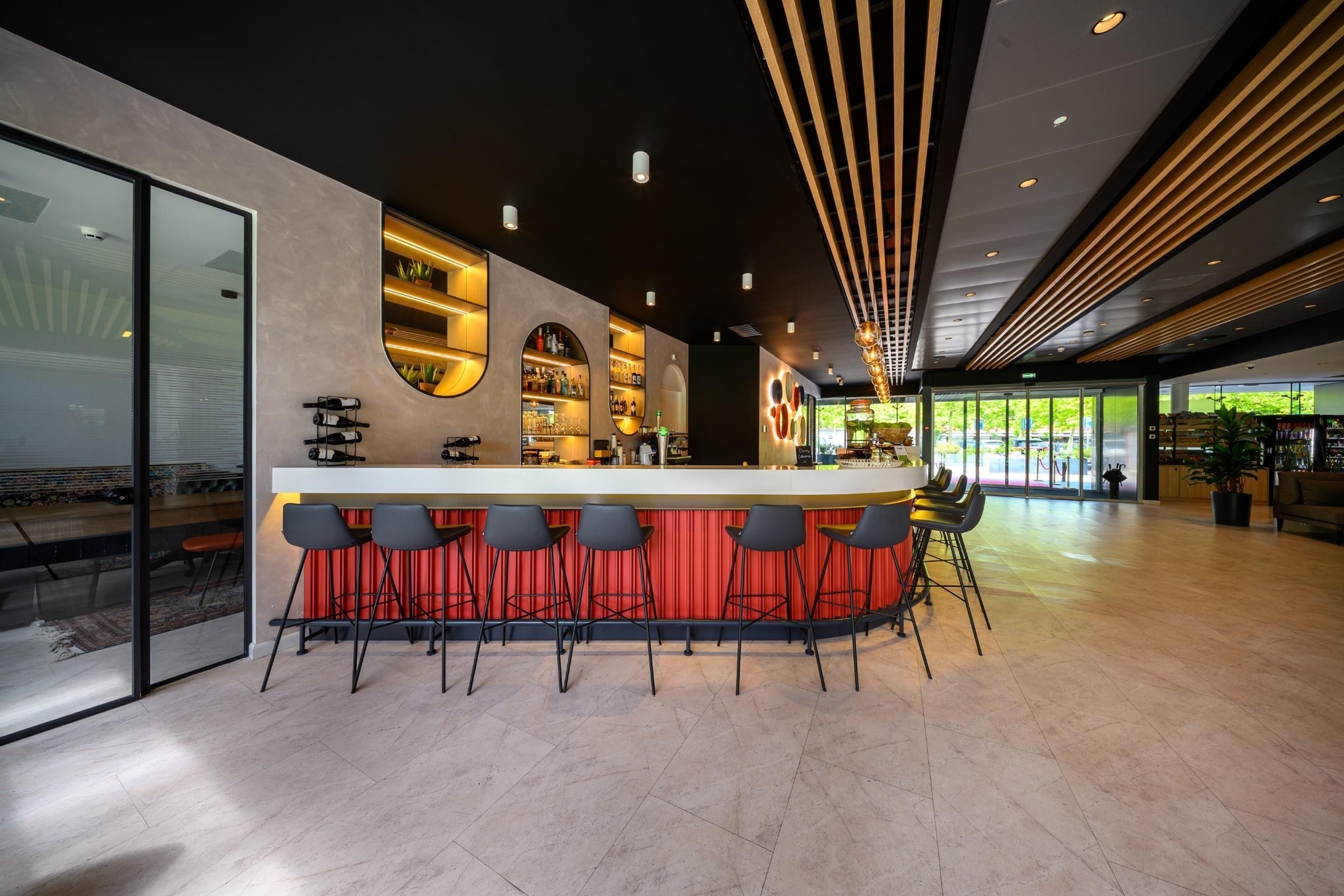 A modern bar area with a counter, bar stools, and shelves stocked with bottles.