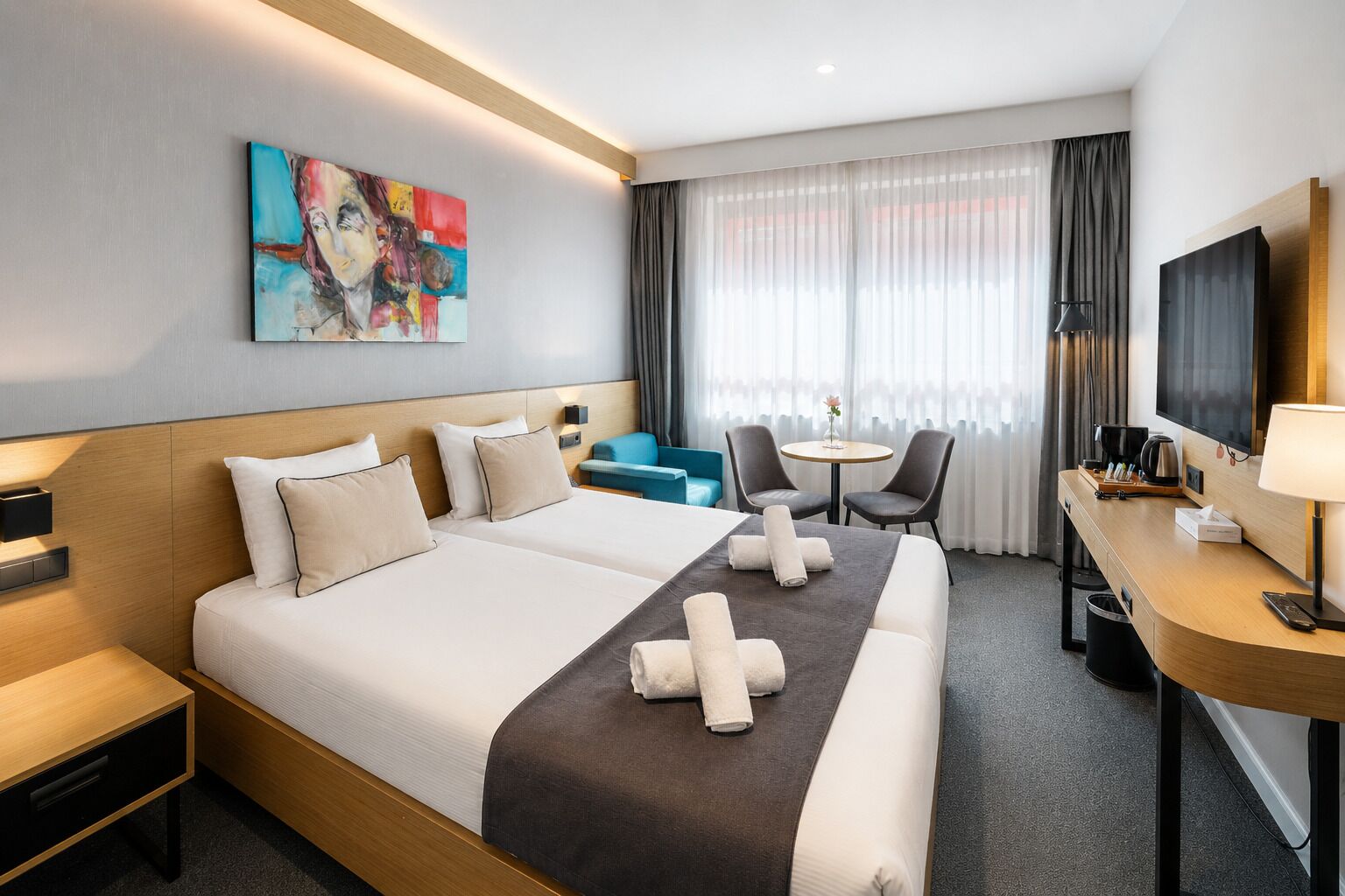 Ein Hotelzimmer mit einem großen Bett, einem Schreibtisch mit Fernseher, einem kleinen Tisch mit Stühlen und einem Bild an der Wand.