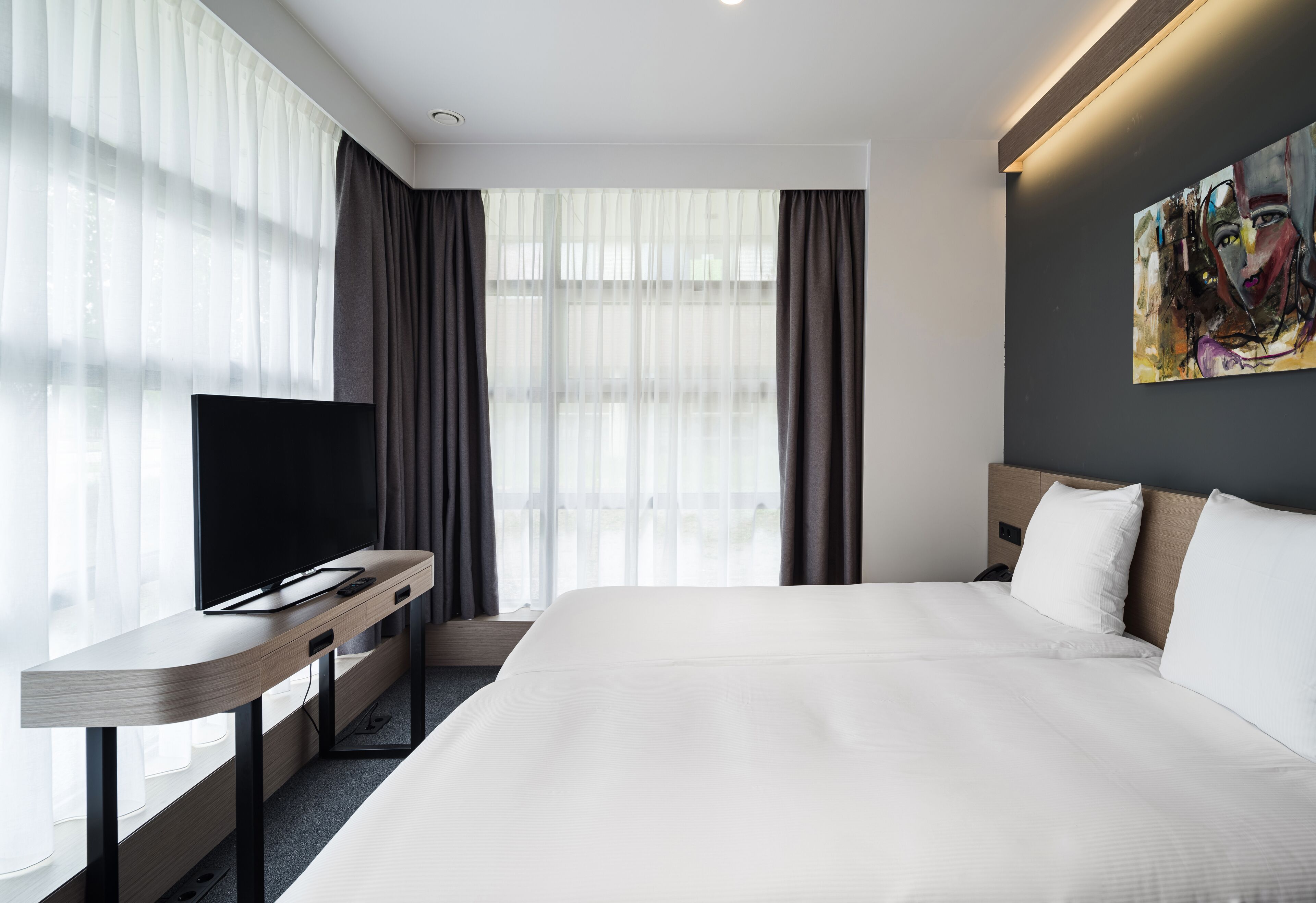 Une chambre d’hôtel moderne avec un grand lit, un téléviseur à écran plat posé sur un bureau en bois et un tableau accroché au mur.