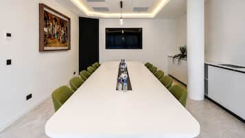 Un salón de conferencias con una larga mesa, sillas verdes, un cuadro en la pared y un televisor montado sobre la mesa.