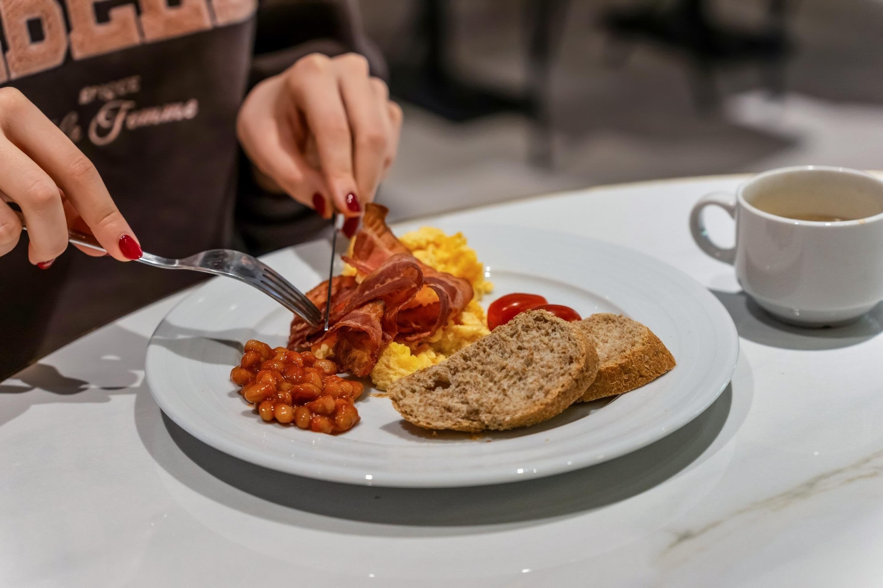 En tallerken med æg, bacon, bønner og ristet brød på et hvidt bord.