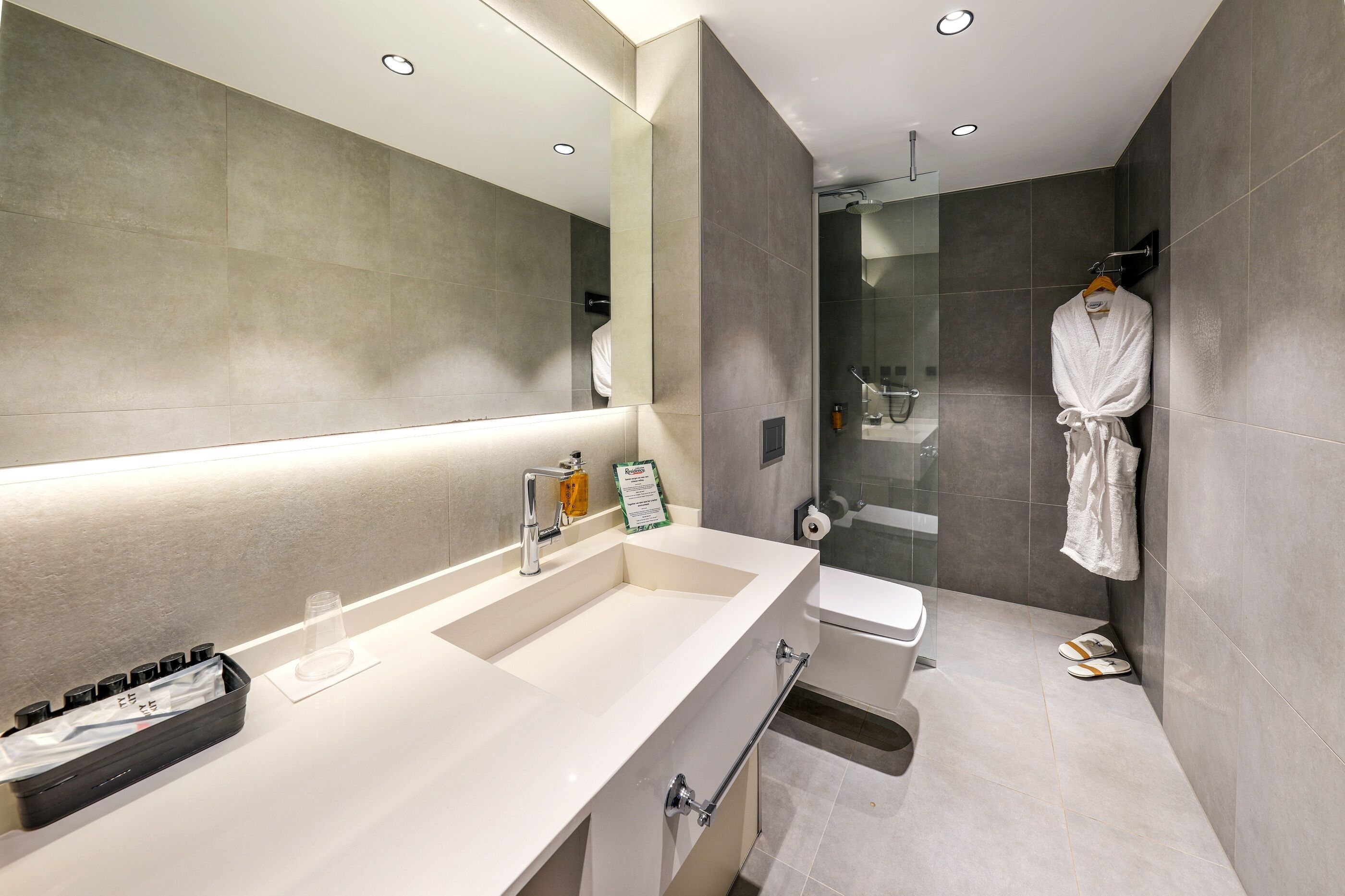 A modern bathroom with a large mirror, a sink, a shower, and a robe hanging on the wall.