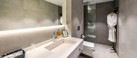 A modern bathroom with a large mirror, a sink, a shower, and a robe hanging on the wall.