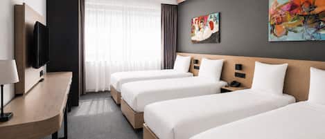 A hotel room with three beds, a desk, a flat-screen TV, and artwork on the walls.