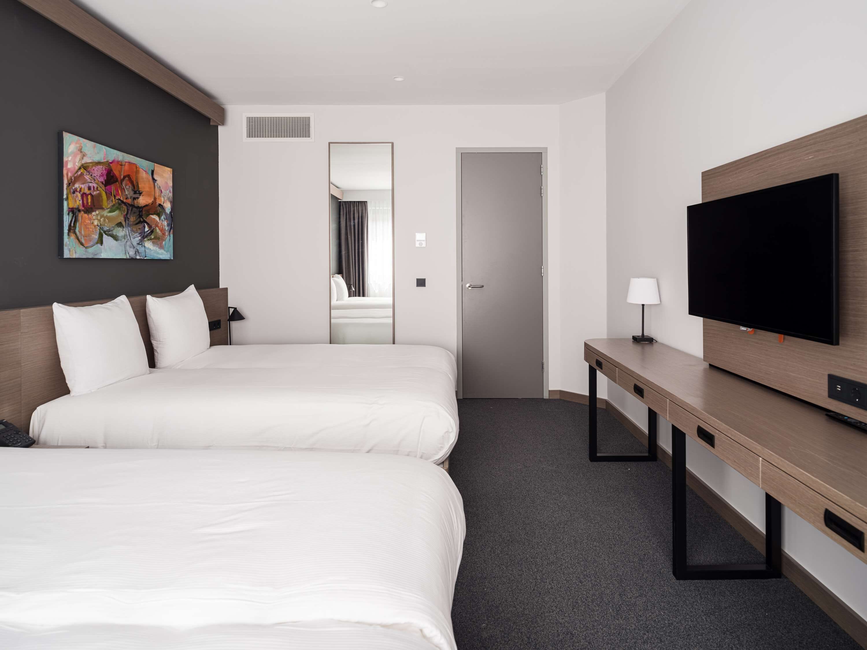 A hotel room with two beds, a TV, a desk, and a painting on the wall.