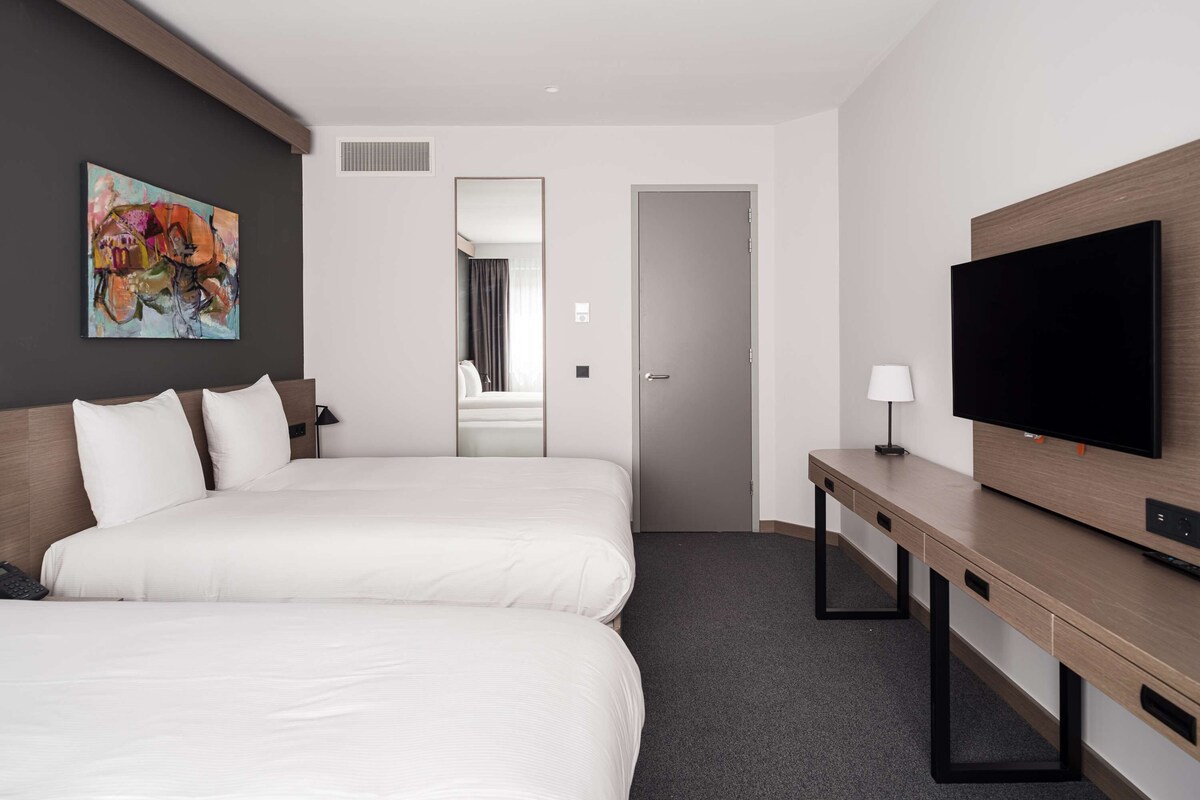 Une chambre d’hôtel avec deux lits, une télévision, un bureau et un tableau au mur.