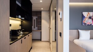 A modern hotel room with a kitchenette, a bed, and a painting on the wall.