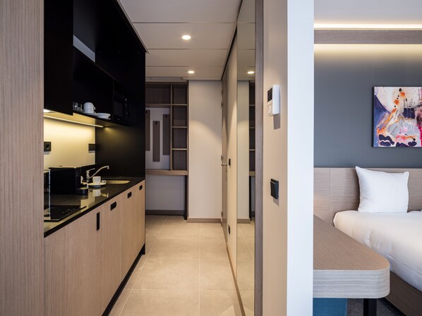 Une chambre d’hôtel moderne équipée d’une kitchenette, d’un lit et d’un tableau au mur.