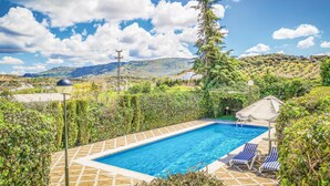Una piscina rettangolare con bordo piastrellato, circondata da vegetazione lussureggiante e un cielo azzurro terso.
