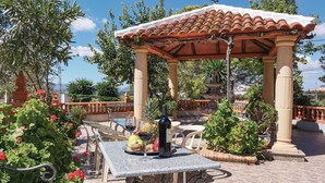 Un gazebo con tetto in tegole, circondato da piante in vaso e un tavolo con una bottiglia e un bicchiere.
