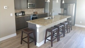 Cozinha moderna com bancadas de granito, eletrodomésticos de aço inoxidável e uma ilha central com banquetas.