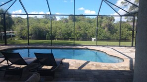 Área de piscina com estrutura de vidro, espreguiçadeiras e vista para um jardim ajardinado.