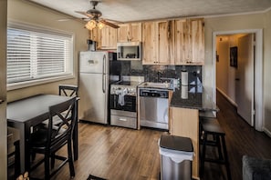 A compact kitchen with wooden cabinets, stainless steel appliances, a dining area with a table and chairs, and a ceiling fan.