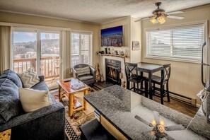 A living room with a fireplace, a dining area, and a balcony with a view of the city.